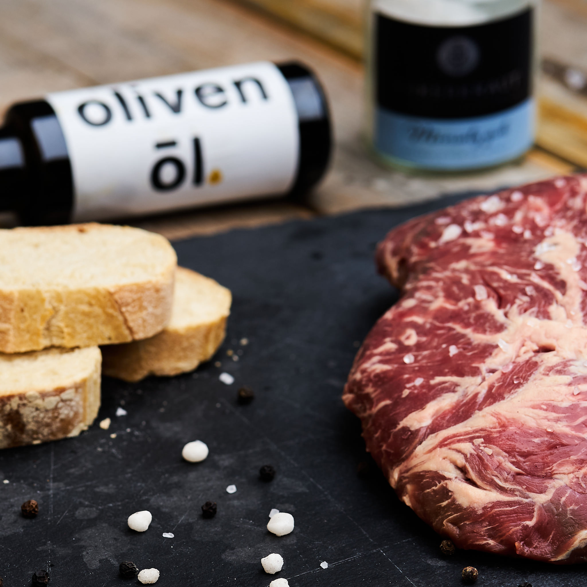 Fledermaus Steak auf schwarzer Steinplatte mit frischem Weissbrot und einer Flasche Fitmeat Oel