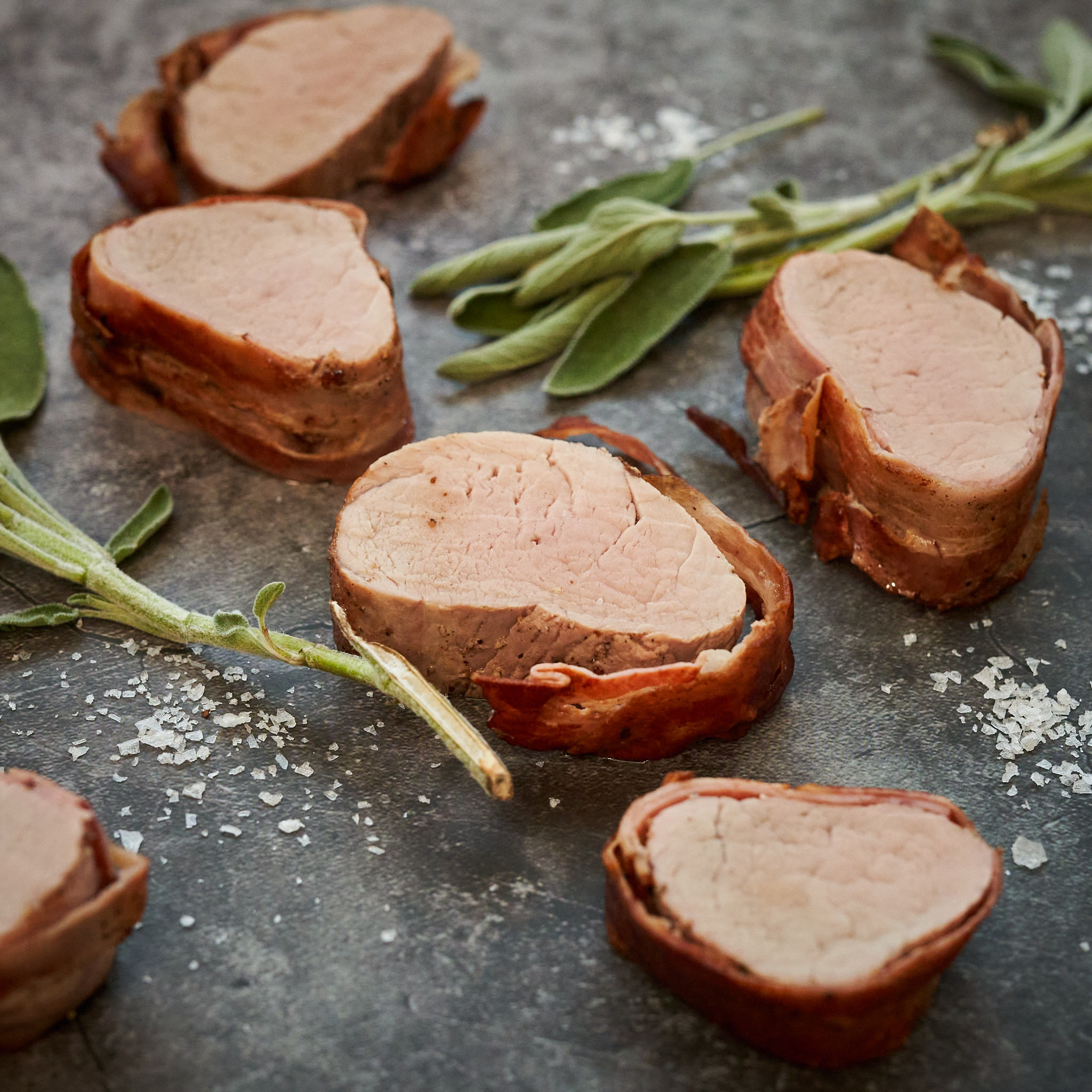 Gebratene Filetstücke vom Strohschwein auf Marmorplatte mit Salbei-Büdel arrangiert 