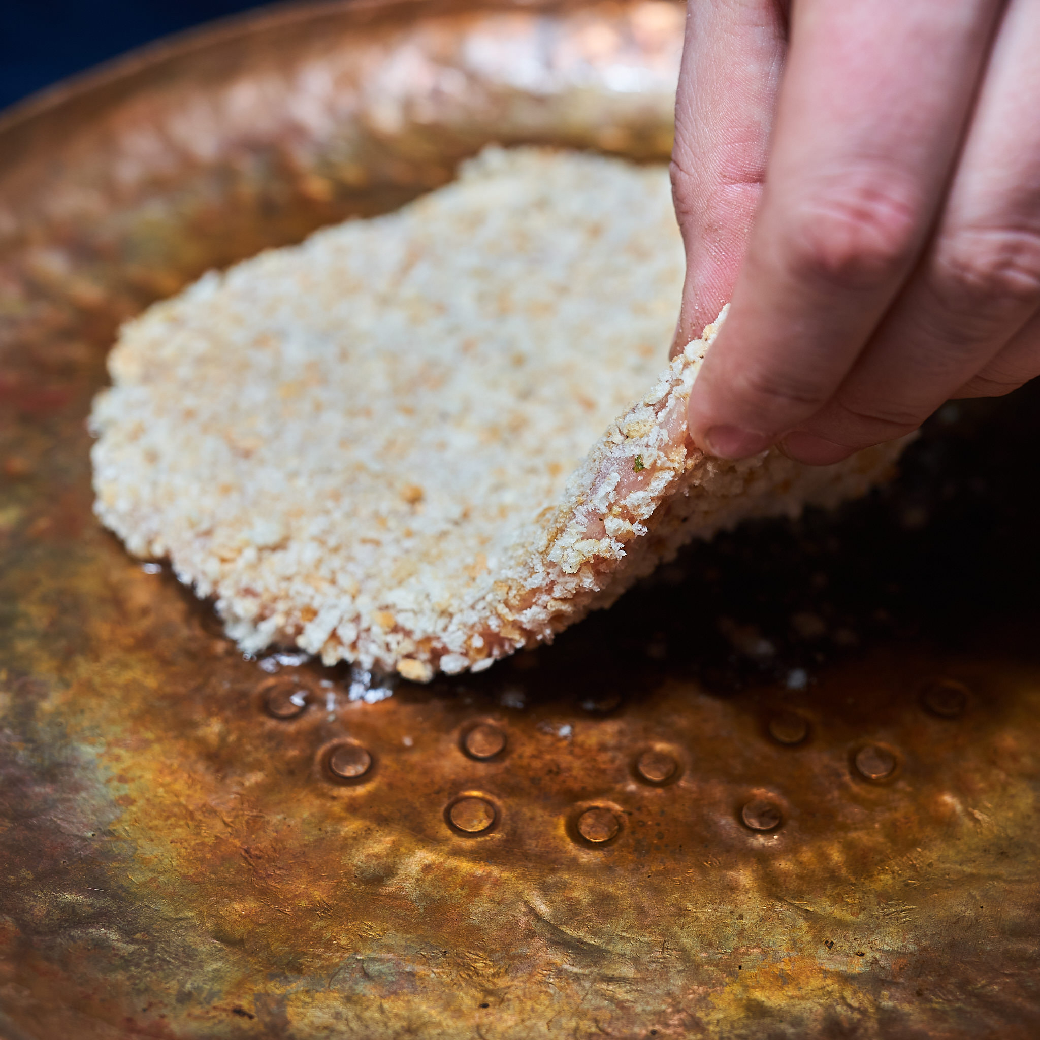 Paniertes Kaiserschnitzel von der Schale wird in Pfanne gelegt
