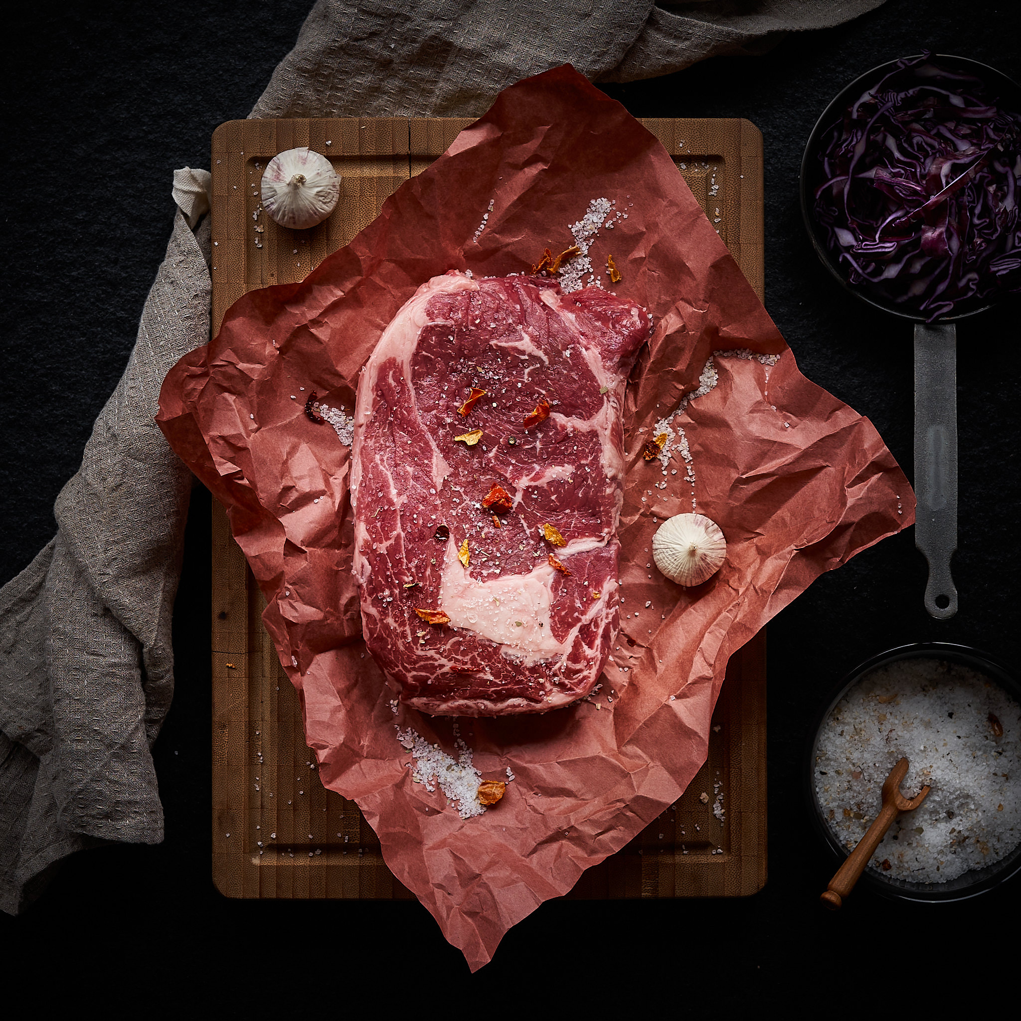 Rib Eye Steak auf rotem Tuch mit Knoblauchzehen und Meersalz