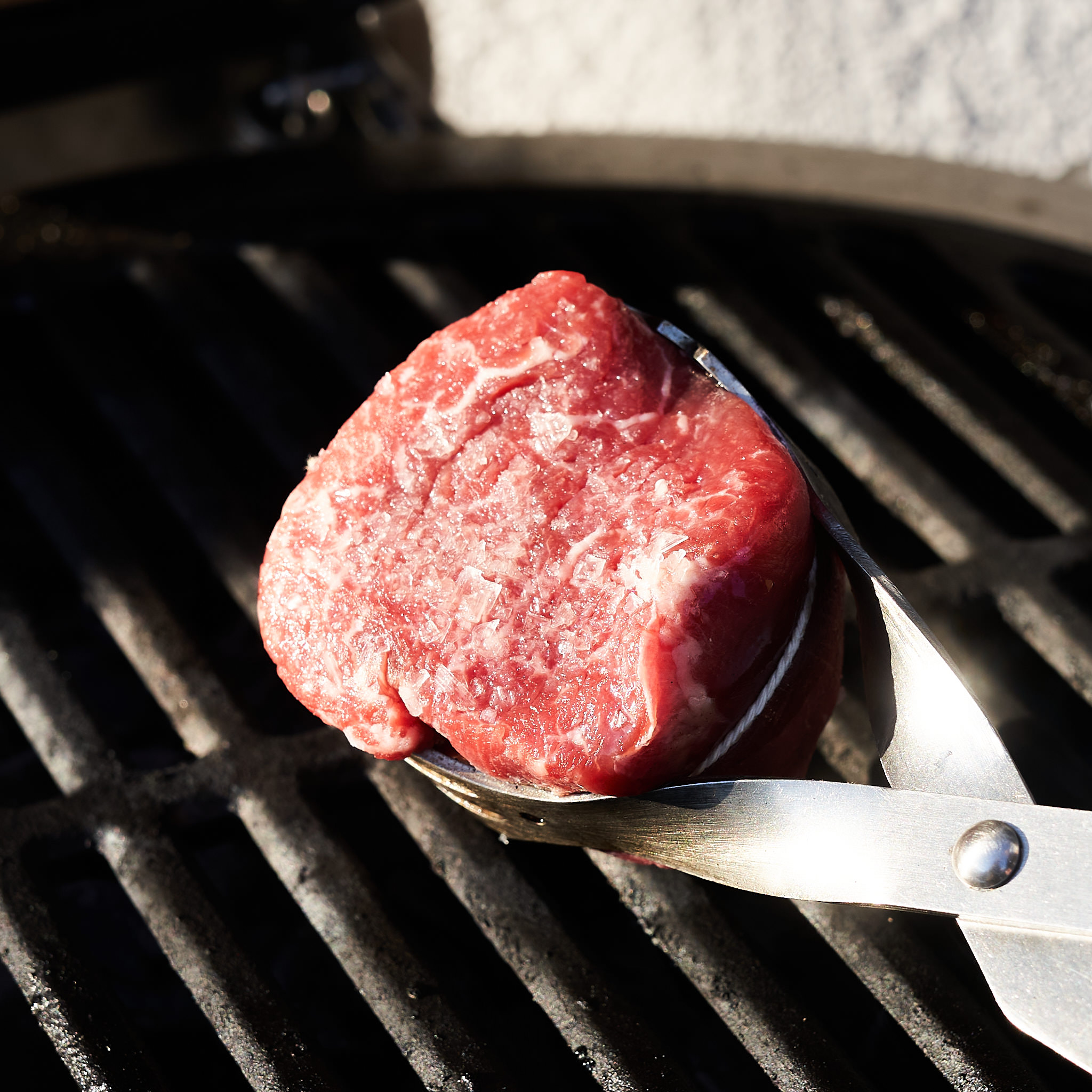 Rinderfilet wird mit Grillzange auf Grillrost gelegt