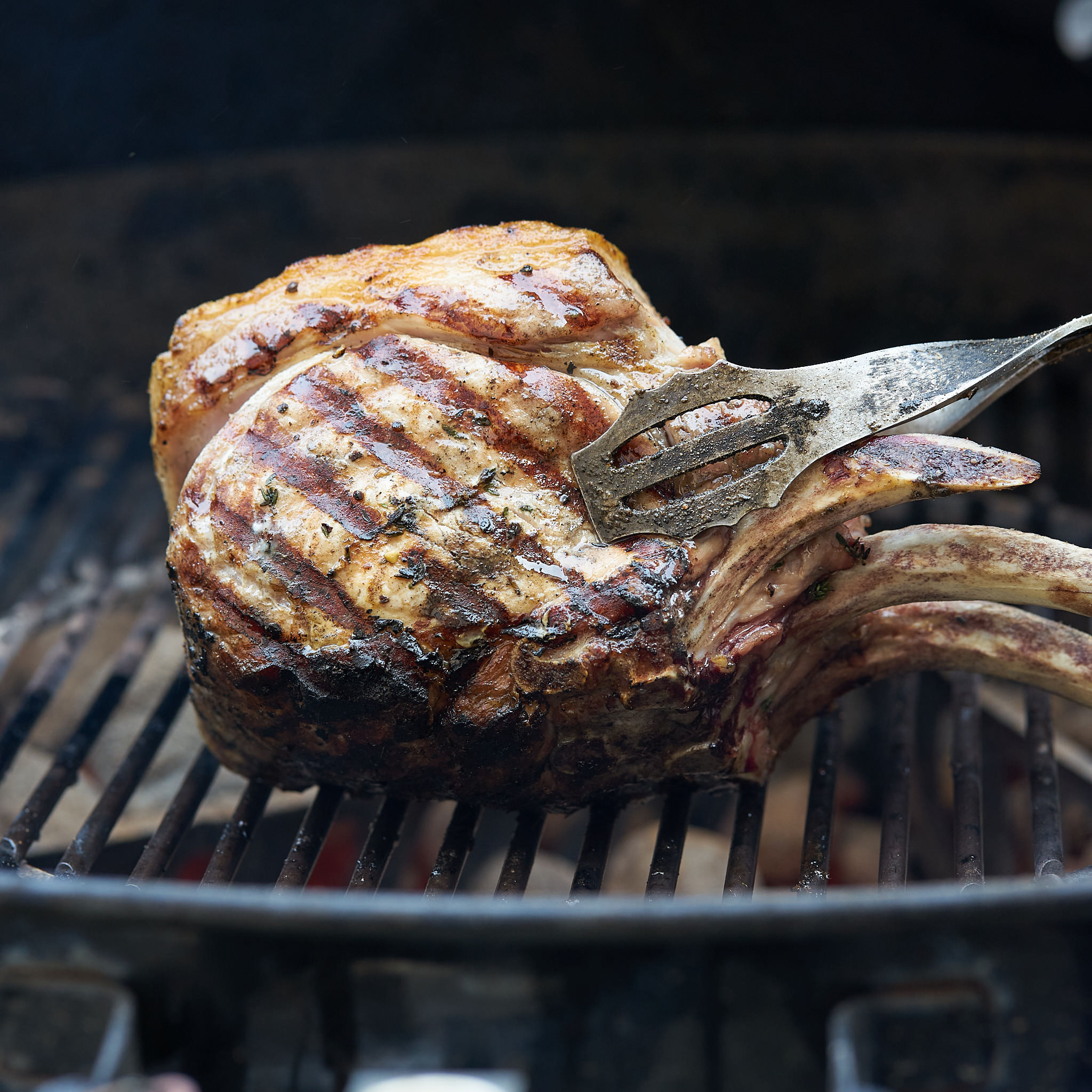 Gegrilltes Tomahawk-Steak vom Strohschwein wird auf Grillrost gewendet