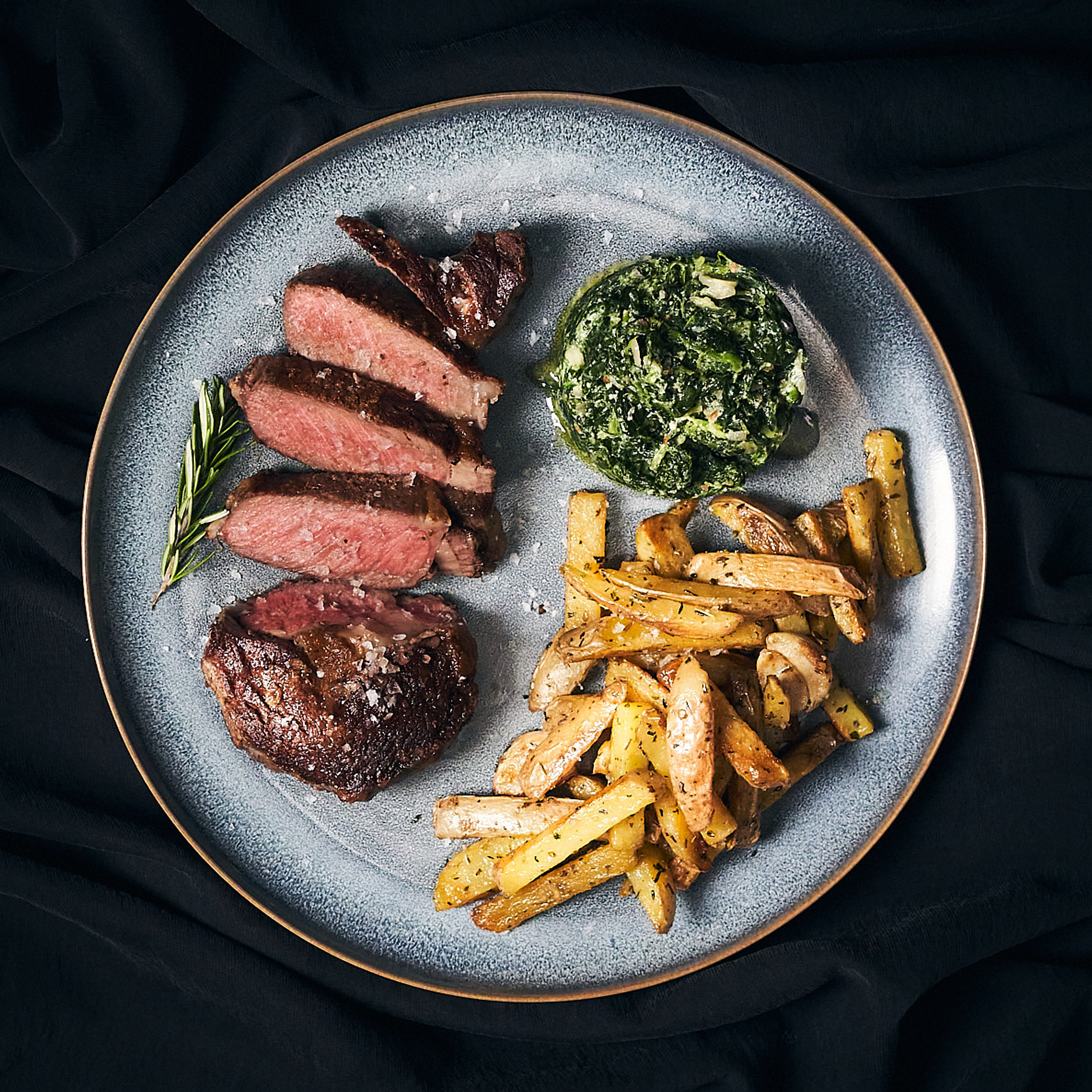 Gegrilltes Rib-Eye Steak mit rosa Kern serviert mit Steak-Fries und Spinat