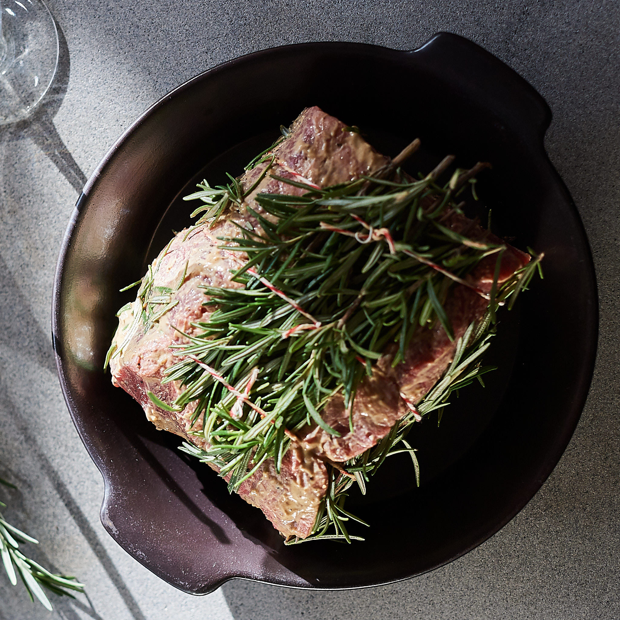 Rumpsteak mariniert mit frischem Rosmarin in schwarzer Schuessel auf Steinbrett