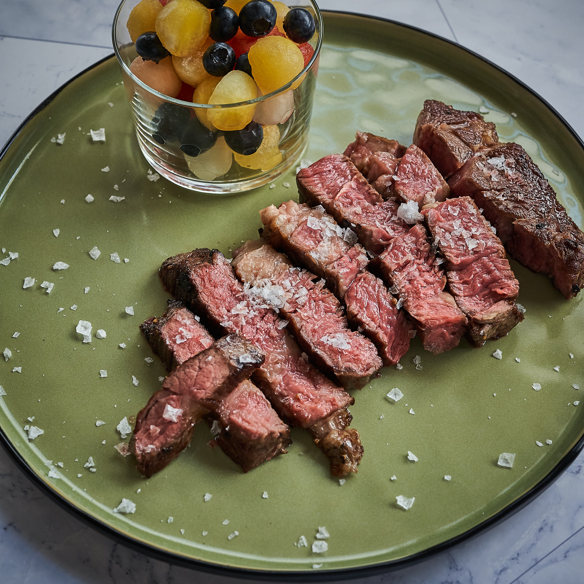 Tranchiertes Chuck Steak auf gruenem Teller mit grobem Meersalz verfeinert
